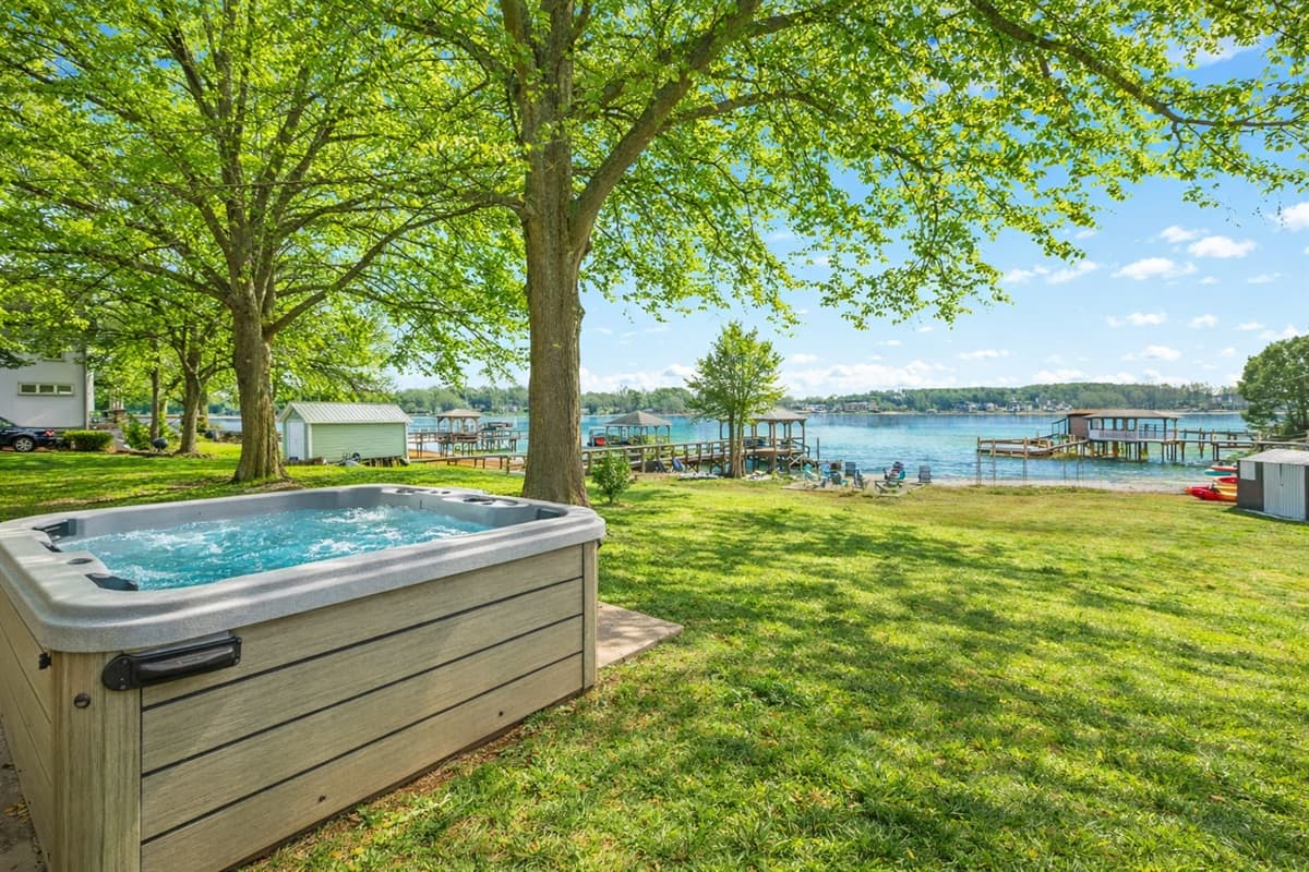 Soak in the hot tub set in the open yard, with the lake visible in the distance.