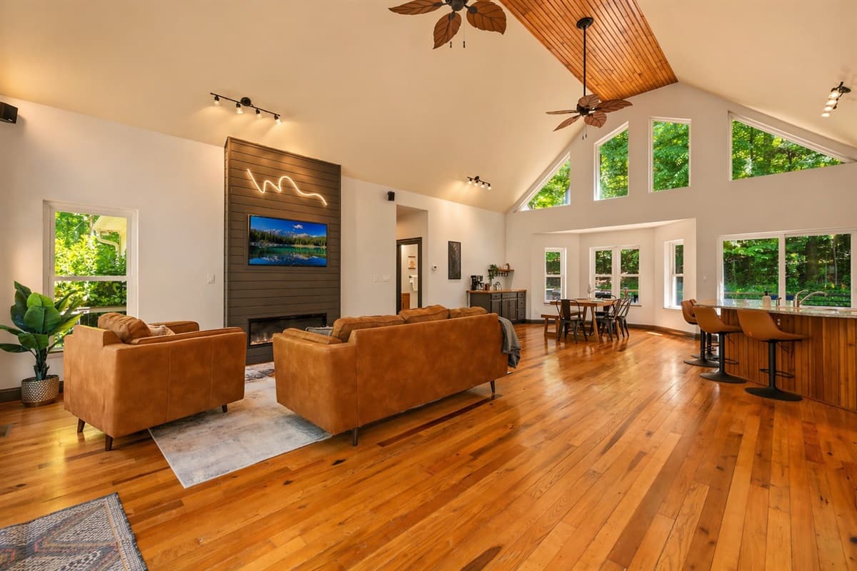 Soaring vaulted ceilings above this cozy space and wall-to-wall windows fill the living room with natural light over leather sofas and a mounted TV.