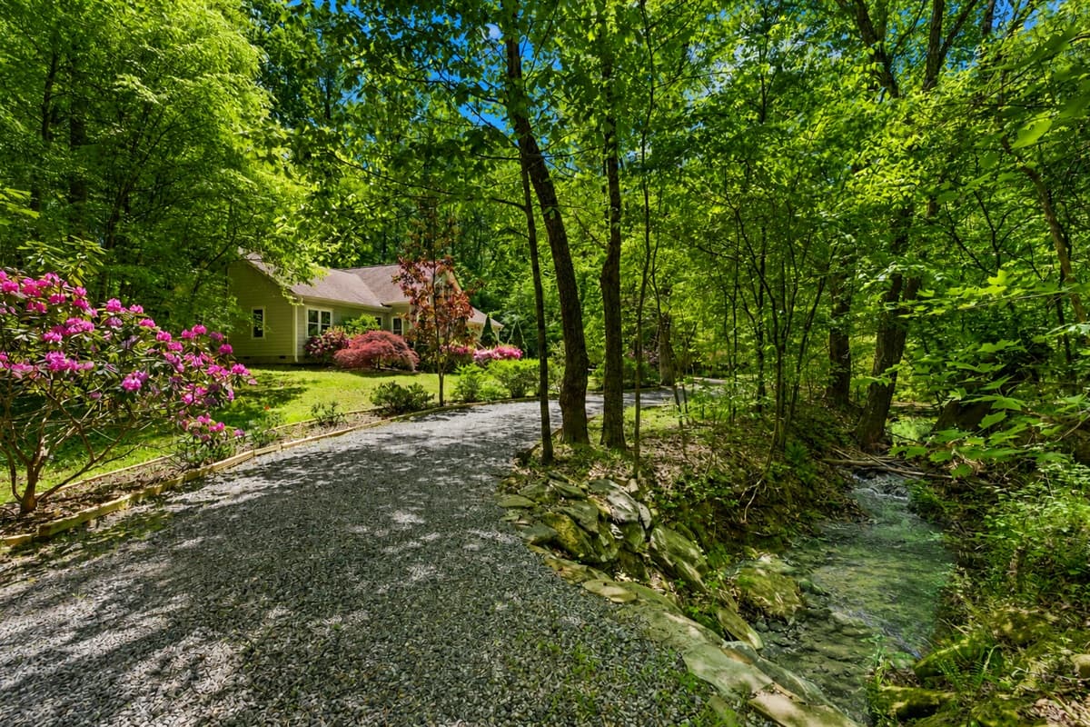A shaded gravel driveway winds past blooming azaleas and a babbling creek, setting a peaceful tone before you even reach the front door.